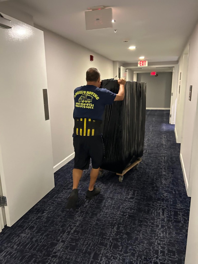 Angel's mover rolling wrapped luxury furniture down building hallway